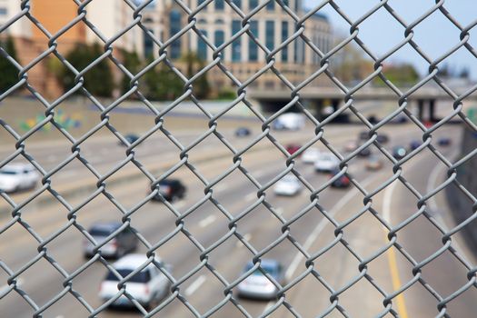 Narrow Depth of Field close up image of chain link fence with out of focus highway and cars