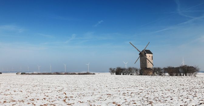 Winter landscape in the central region of France, with a traditional wooden windmill and some modern windturibines in the distance.