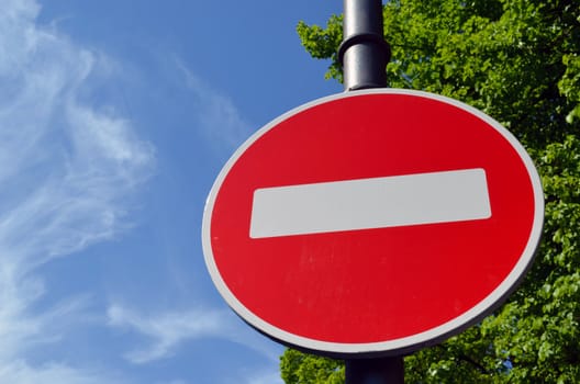 Limiting traffic sign white brick on red round background against blue sky and green trees.