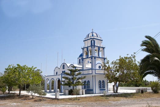 A Blue and White Greek Orthodox Church and Bell Tower surrounded by Trees