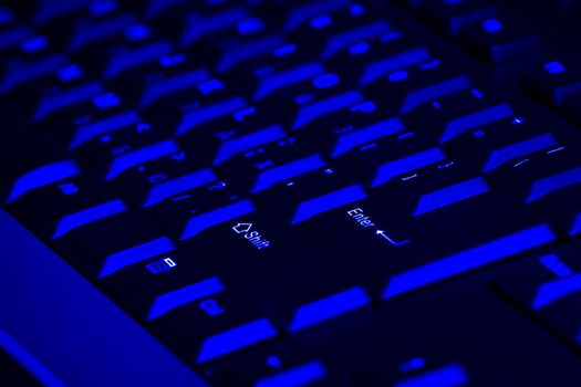 fragment of keyboard from the corporate computer of dark color illuminated from beneath light with a blue tint