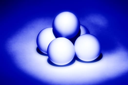 four white balls for table tennis built a pyramid and illuminated from beneath blue light