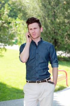 Unhappy young man in park with telephone