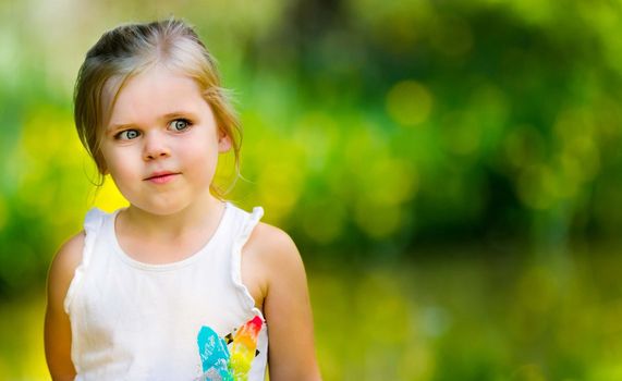 Young girl is against a green background with yellow highlights. lots of open copy space and girl is looking into the blank area. Image has a very shallow depth of field with focus only on the girl