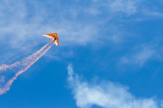 Hang glider with smoke trails and streamers against a blue sky with some cloud cover. Lots of copyspace available