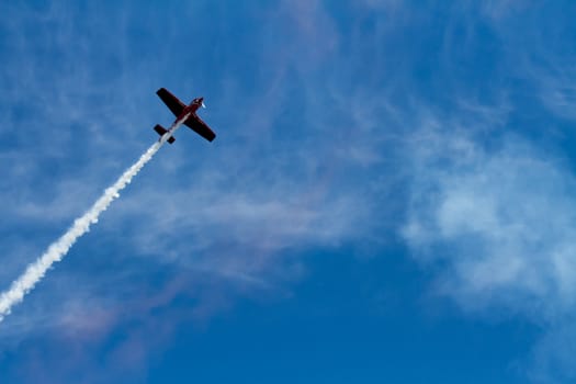 A plane that is heavily backlit almost creating a silhouette against the summer sky. Smoke is comming from the plane and clouds are visable in the sky.