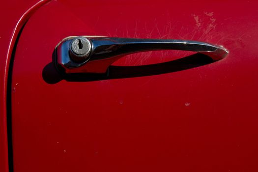 A red car door with a vintage metal handle and push button opener with a key hole lock.