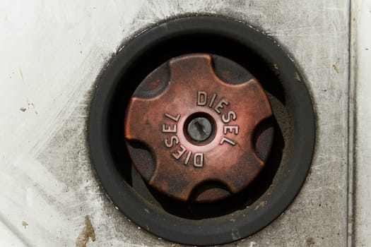 A faded red diesel fuel cap with key lock inset in a rubber housing with grimy white paintwork surrounding.