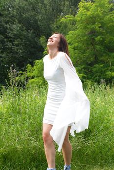 young happy caucasian brunette woman in white dress laughing in green park outdoor