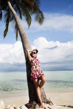 Carefree young woman relaxing with her back to a palm tree on a sandy tropical beach while enjoying an island vacation