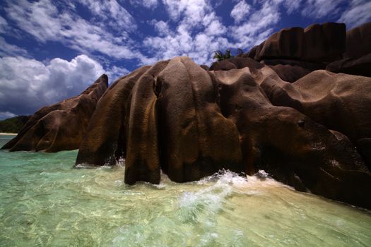 Blue sky laced with fluffy white clouds over a beautiful shore lined with smooth weather worn boulders