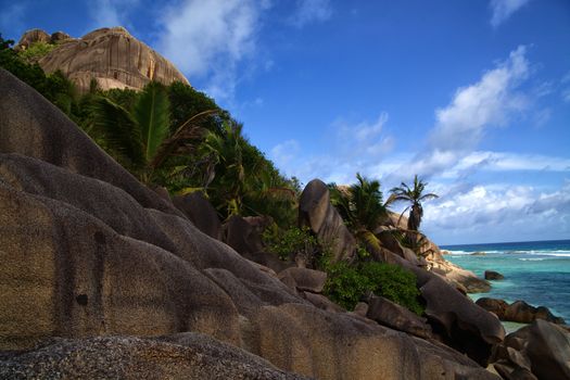 Steep rocky shoreline leading to the ocean beach under a tropical sky
