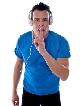 Handsome young male enjoying music and showing you silence gesture
