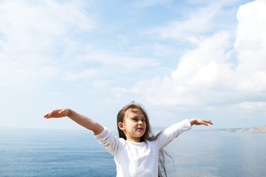 girl in a white jacket standing arms outstretched to the side against the sea