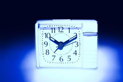 the alarm clock of white color is illuminated from beneath dark blue by light on a white background