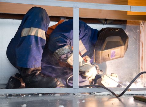 Welder working in cramped conditions in an uncomfortable position while lying on the floor