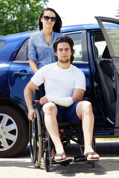 Young couple leaving or arriving to the hospital,young man in wheelchair with a cast on his hand.