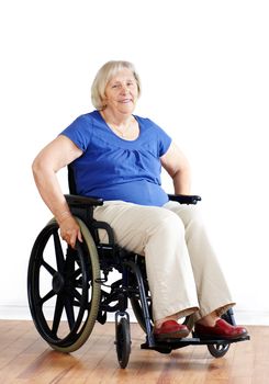 Smiling senior woman seated in a wheelchair, either handicapped or disabled, looking at camera over neutral white background.