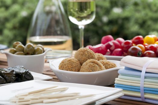 Summer tapas table with bitterballen in focus, and wine, olives and radishes in the background