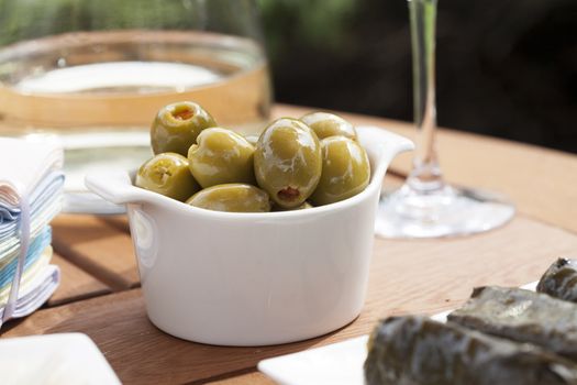 Green olives stuffed with red pimento in small white bowl.