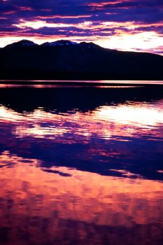 Reflection of beautiful sunset sky over silhouette of rural wilderness mirrored on calm surface of lake