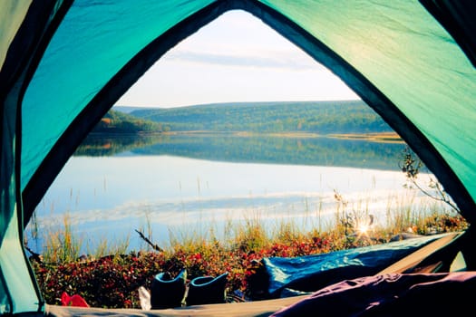 Looking out of open tent door upon calm lake in morning sunshine.