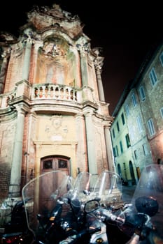 Bunch of motor scooters parking in front of historic house downtown Siena, Tuscany, Italy, Europe, at night.