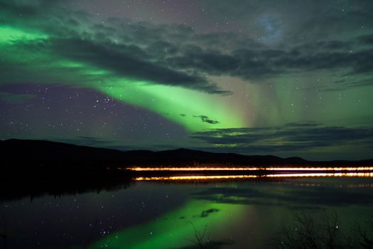 Night Sky Stars, clouds and Northern Lights over country road at lake shore, Yukon, Territory, Canada.