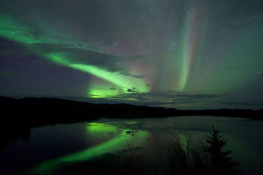 Night Sky Stars, clouds and Northern Lights over country road at lake shore, Yukon, Territory, Canada.
