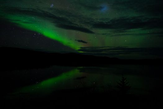 Night Sky Stars, clouds and Northern Lights mirrored on calm lake in Yukon, Territory, Canada.
