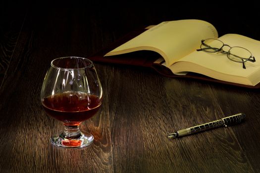 A glass with cognac, cigar and an old book nearby