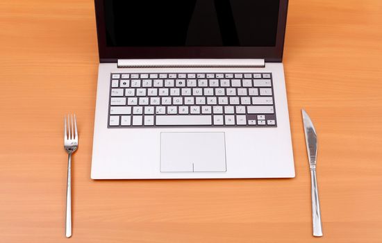 Laptop computer with fork and knife on the table