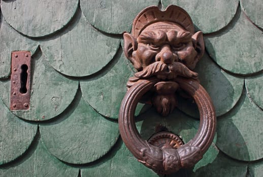 Old green door in Pisa, Italy with am aged rusty handle and key hole. 