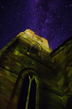 Low angle view of a stone church tower with decorative windows reaching up towards a starry night sky