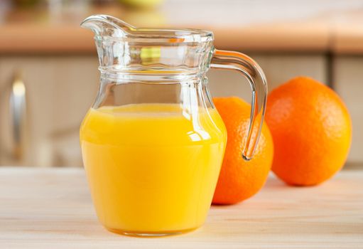 Fresh orange juice in glass jar with oranges lying on table.