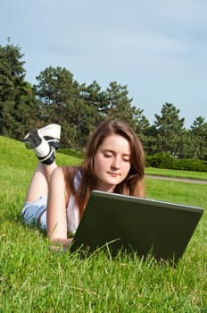Woman with laptop lying on grass in park.
