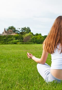 Woman meditating sitting on grass in garden. View from back.