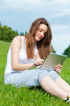 Girl working with tablet sitting in park on gras.