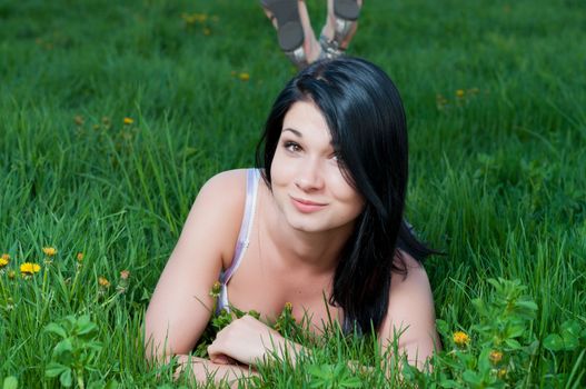 Smiling woman lying on grass with dandelions.