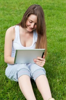 Girl sitting on grass with tablet in his hands. 