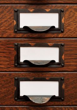 Vertical stack of three small, old oak flat file drawers with white empty tags in tarnished brass label holders.