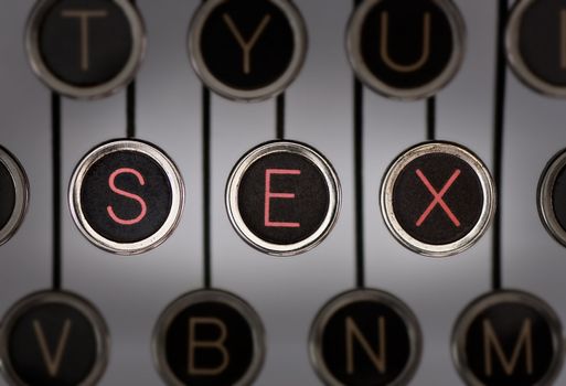 Close up of old typewriter keyboard with scratched chrome keys with black centers and white letters. Lighting and focus are centered on for keys spelling out "SEX". 