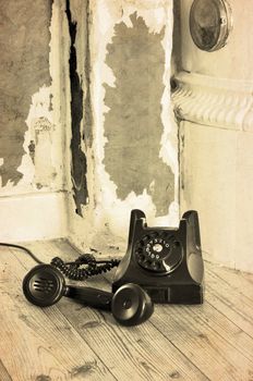 Old black bakelite phone on the floor in a grungy house with the receiver off.