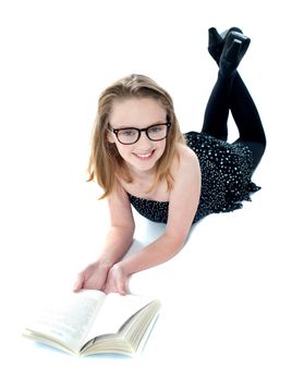 Smiling little girl lying with an open book on floor. All on white background