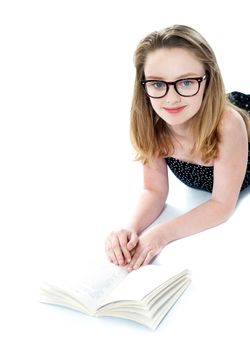 Girl wearing eyeglasses and reading book. Lying on white floor