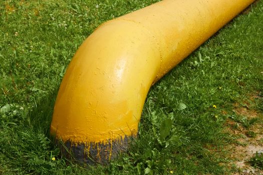 Large natural gas pipe comes out of the ground among the green grass