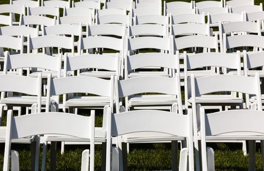 Rows of formal white wooden wedding chairs set up for a wedding or concert