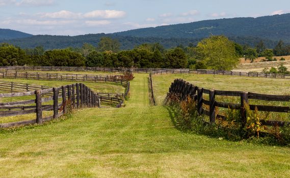 Green pasture land with wooden fences and hills in background