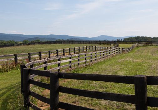Green pasture land with wooden fences and hills in background