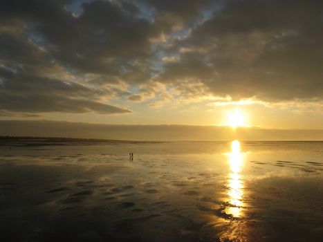 Sunset view of the ocean shore in Southport, UK with a couple walking during a low-tide.